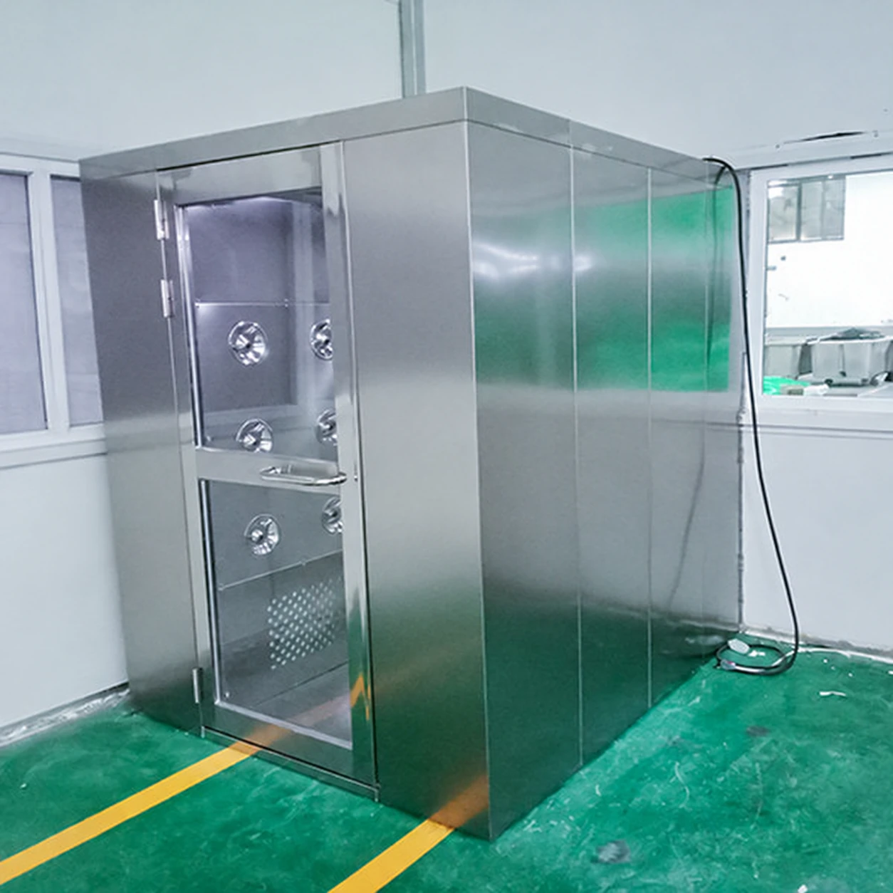 Stainless air shower installed beside a worn green factory floor