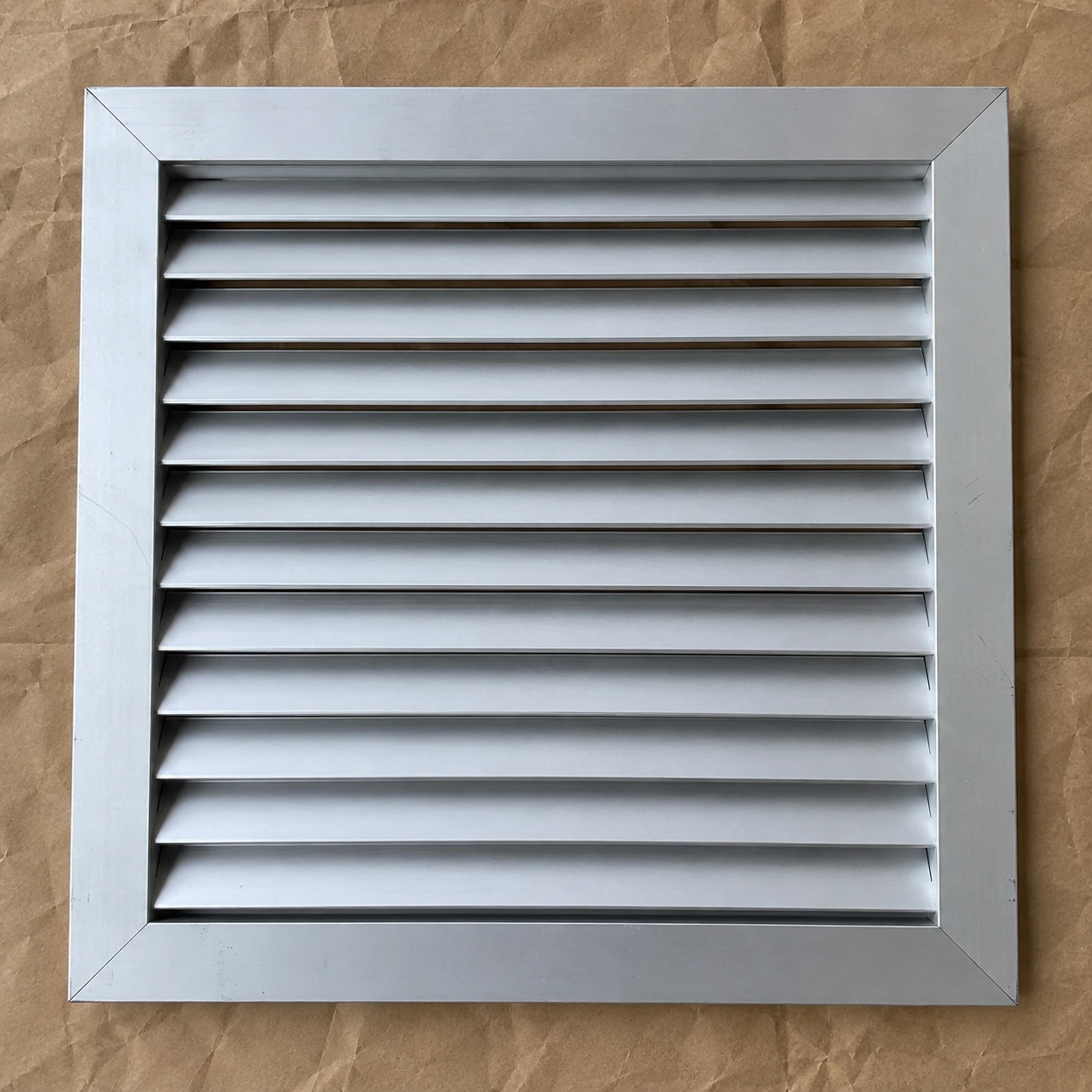 Square anodized aluminium return grille with sloped louvers on packing paper
