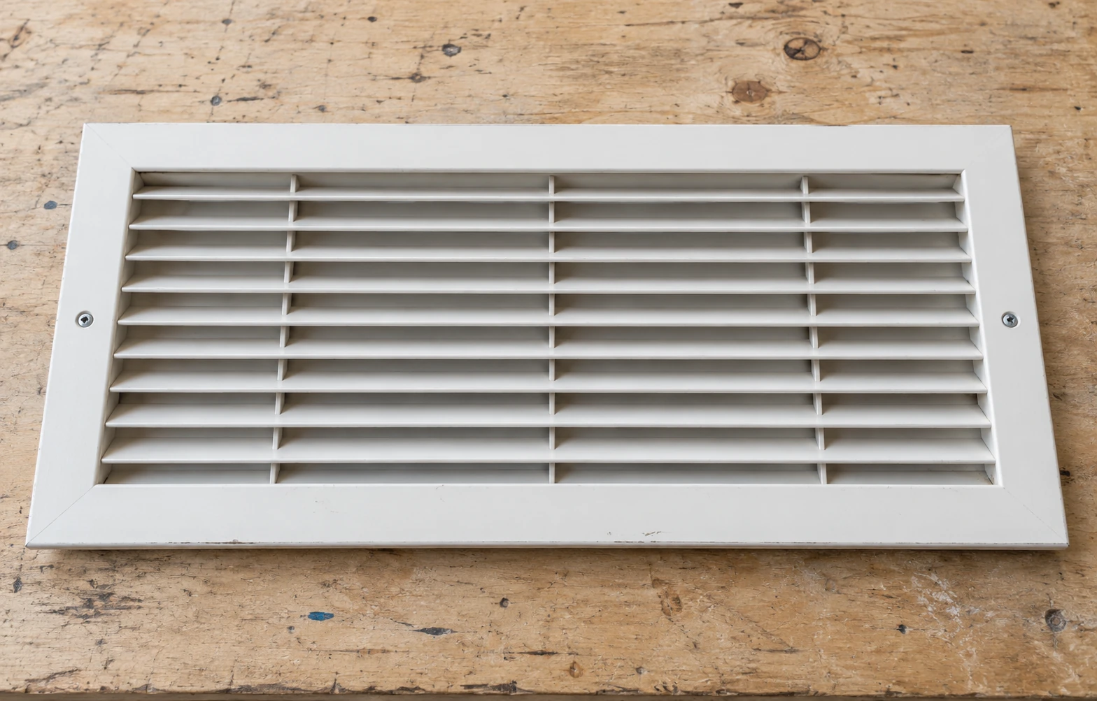 Wide twenty-five-by-sixteen off-white return grille on a wooden worktable